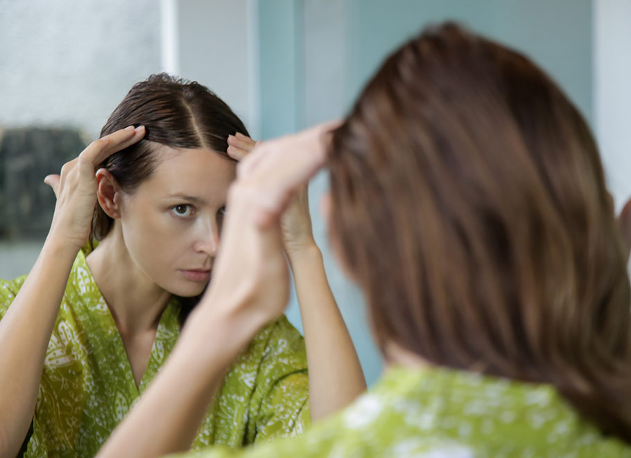 woman looking at hairline in mirror