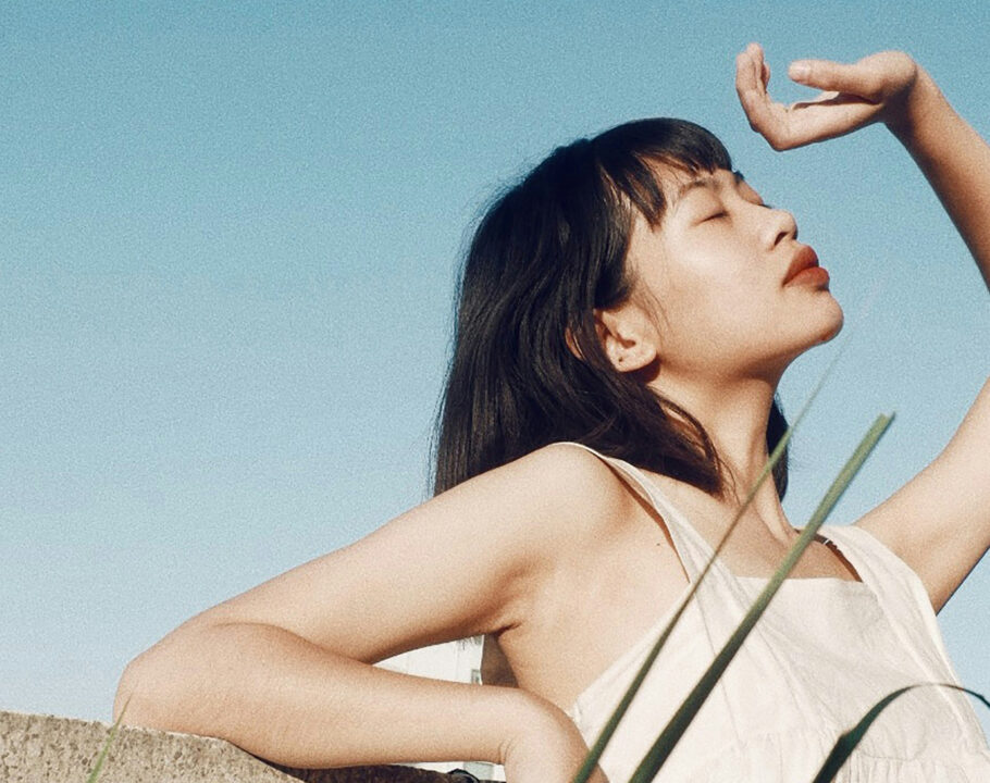 Asian woman outdoors looking up to sky with eyes closed and hand over her face