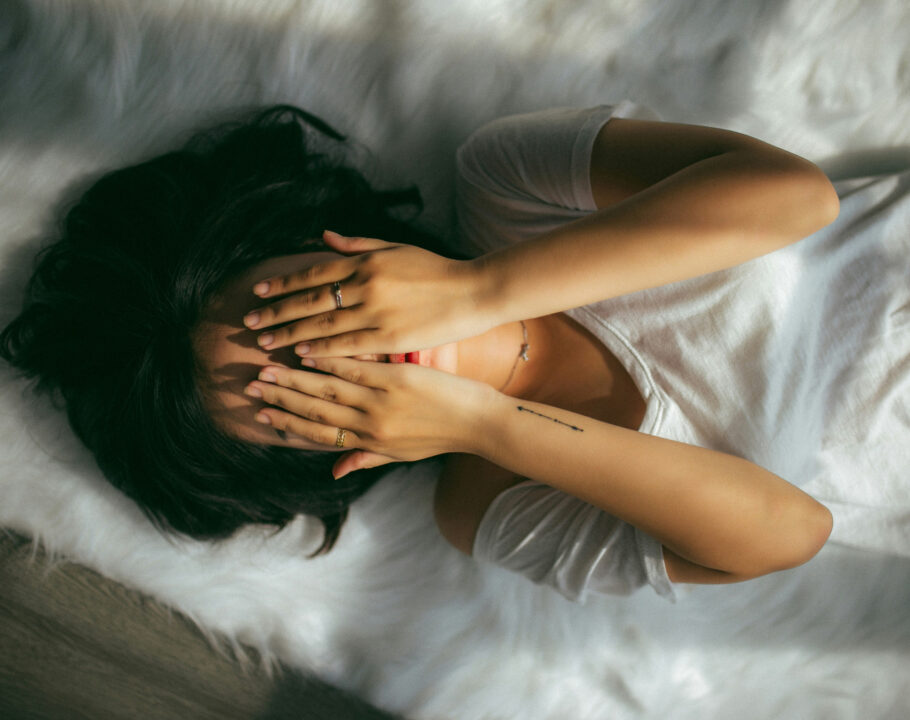 woman lying on bed with hands over her face