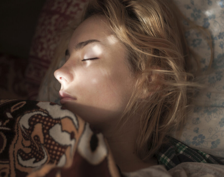 close up of blonde woman sleeping in bed with sunlight on face