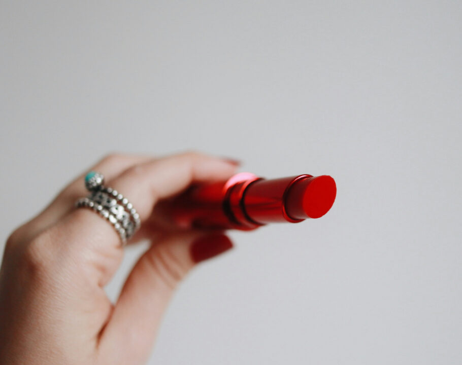 hand holding an open red lipstick against a gray background