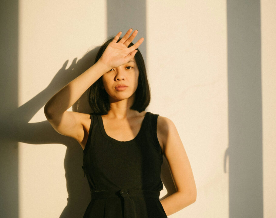 Asian woman in black dress standing in sunset shadows with hand in front of face