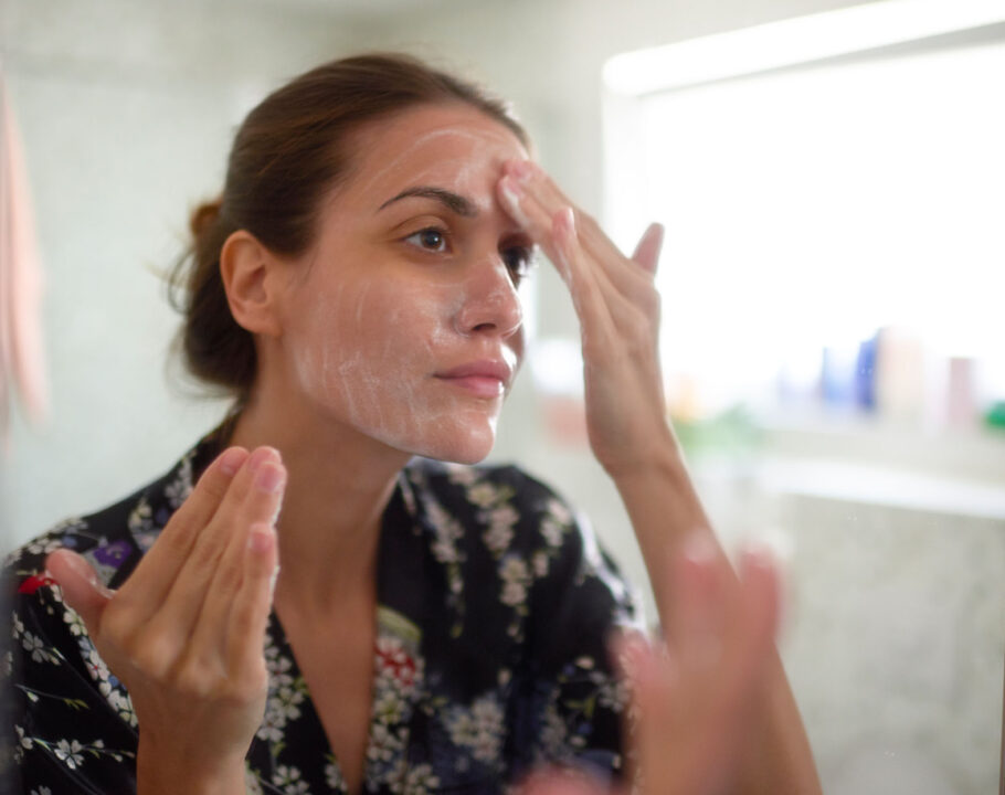 woman applying skin product to face in bathroom