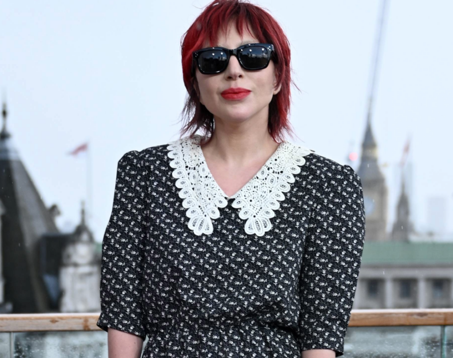 A photo of Lady Gaga with a short haircut and red hair as she stands outside with a cityscape behind her